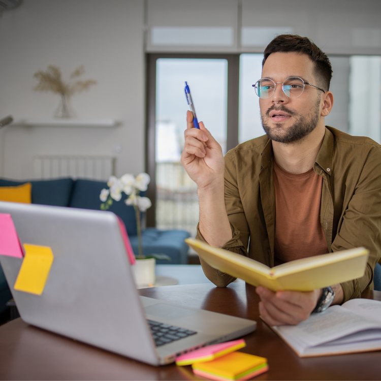 Photo shows a man sitting at a laptop learning and taking notes