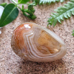 Side view of a banded agate with fine concentric patterns and a standout triangular shape in earthy orange and cream hues.
